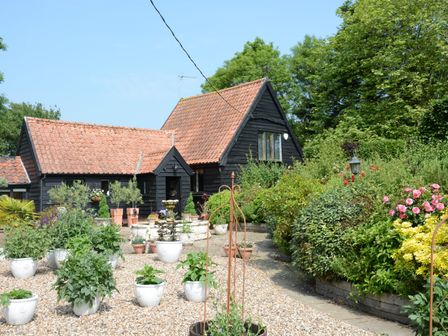 A garden with potted plants flowers and shrubs surrounding a black wooden house with a tiled roof at Wassicks Cottage Haughley