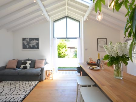 A living area with a gray sofa and pillows next to a wooden counter with stools and flowers at The Curious Oyster Orford