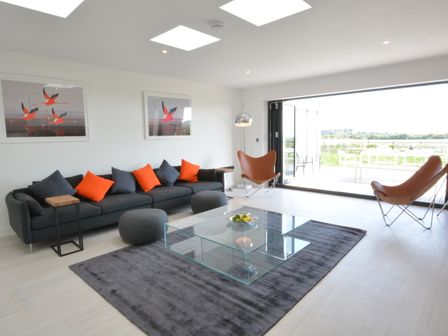 A living room with a dark grey sofa with orange and dark grey cushions two brown chairs and a glass coffee table at Skylight Aldeburgh in Aldeburgh