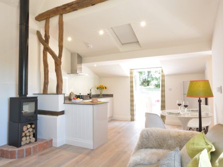 A kitchen and dining area with a wood burning stove and wooden beams at Carriage House Bruisyard Near Framlingham