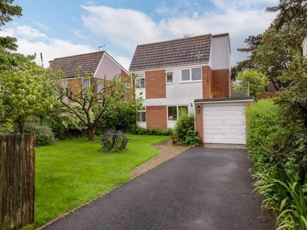A driveway leading to a garage with a two-story house and garden furniture on the lawn at The Bridge House Southwold
