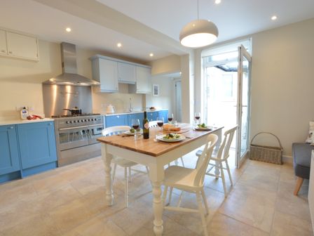 A kitchen with a wooden dining table set with food and wine glasses at Somewhere Only We Know Aldeburgh