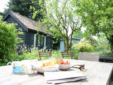 A garden with a wooden table set with mugs bowls of croissants and strawberries and glasses of juice at The White House with Studio in Wortwell