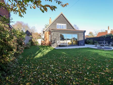 A backyard with a house featuring a large window and wooden bench at Mellows Thorpeness in Thorpeness