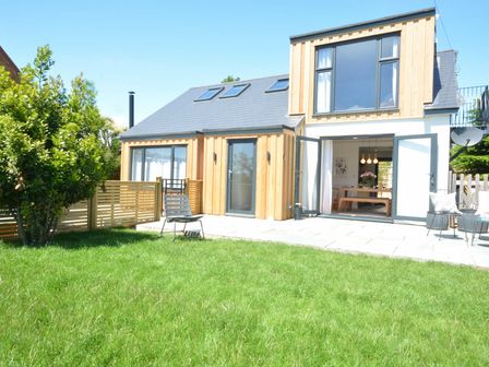 A modern house with wooden panels a green lawn and outdoor chairs at The Dunns Orford