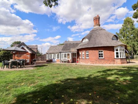 An outdoor area with a thatched house and patio seating at The Round House in Easton near Framlingham