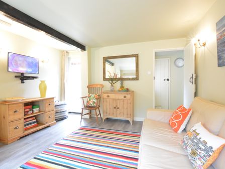 A living room with a beige sofa and cushions a wooden chair a wooden cabinet with a mirror above and a colorful striped rug at Church Farm Cottage Dunwich Near Westleton