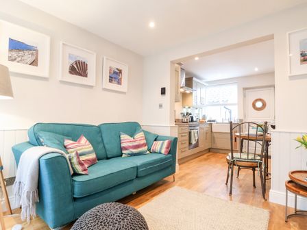 A living room with a teal sofa and striped pillows next to an open kitchen with wooden flooring at 51 Tern Cottage Aldeburgh