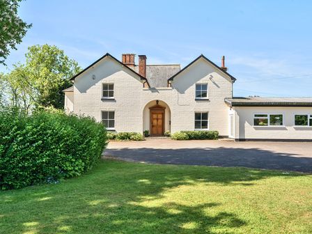 A white two-story house with a central wooden door and windows surrounded by greenery at Bedingfield House nr Debenham Debenham