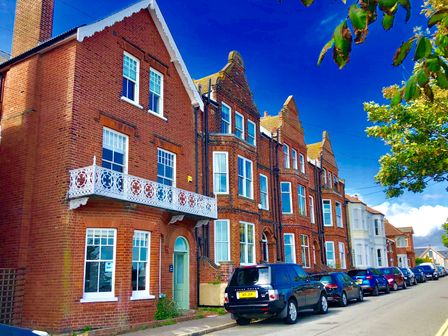 A street with parked cars and brick houses under a blue sky in Aldeburgh