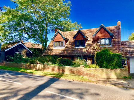A house with tiled roof, dormer windows, brick wall, and trees along a road at Town Farm House Orford