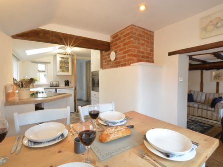 A dining table set with plates and glasses of wine near a kitchen with wooden beams and a brick chimney at The Moorings Orford