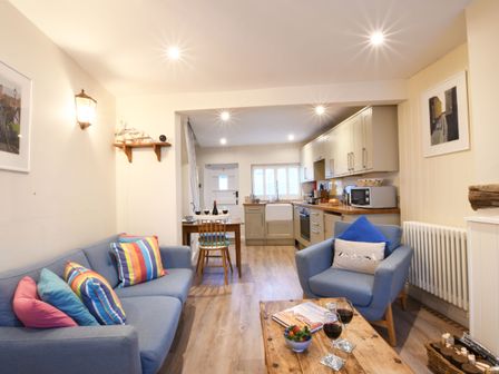 A living room with blue sofas and a wooden coffee table next to a kitchen with cabinets and a dining table at Smugglers Rest Aldeburgh