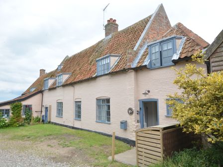 A row of connected houses with tiled roofs blue framed windows and a small garden at Old Valley Farm in Walberswick