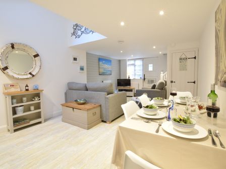 A dining table set with bowls and utensils next to a living area with grey sofas and a television at The Smokehouse Cottage in Southwold