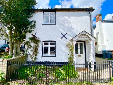 A white two-story house with black window frames and a white door with a small porch surrounded by a black metal fence and green plants at Satis Cottage Westleton