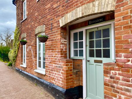 A brick exterior wall with two windows and a green door at Rosedene in Rickinghall