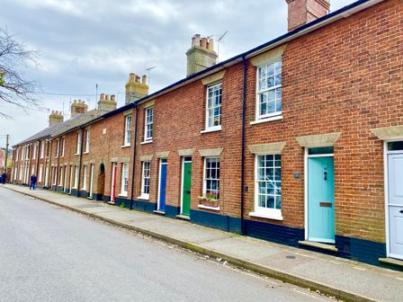 A row of brick terraced houses with multiple chimneys and colored doors on a street at 15 Victoria Street Southwold