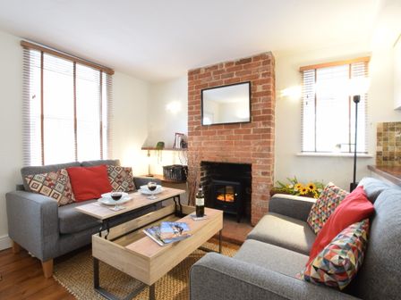 A living room with two grey sofas and a brick fireplace at 1 Tailors Cottage Woodbridge