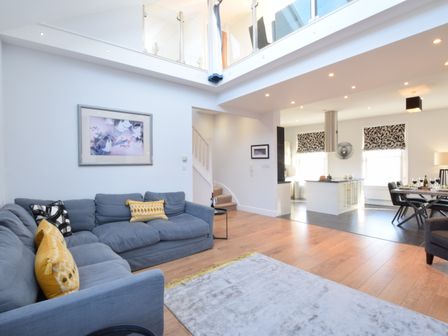 A living room with blue sofas and yellow cushions a carpet and an open kitchen and dining area at Pier View Southwold