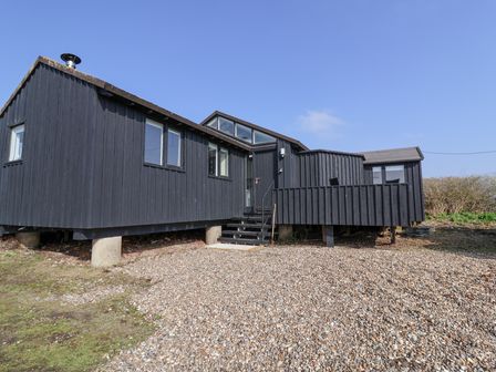 A black wooden elevated house with stairs and a gravel area at The Old Fisherman's Hut in Southwold