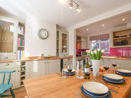 A kitchen with a wooden table set for four with bowls glasses and a vase of white tulips at The Teepee Southwold