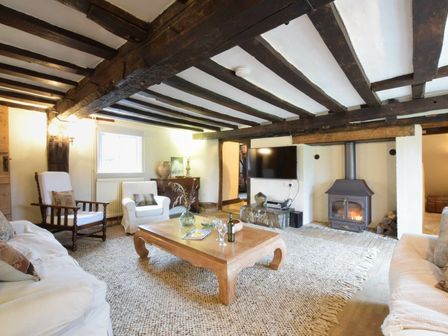 A living room with wooden beams a wood burning stove sofas armchairs and a wooden coffee table at Church Farmhouse Cookley Near Halesworth