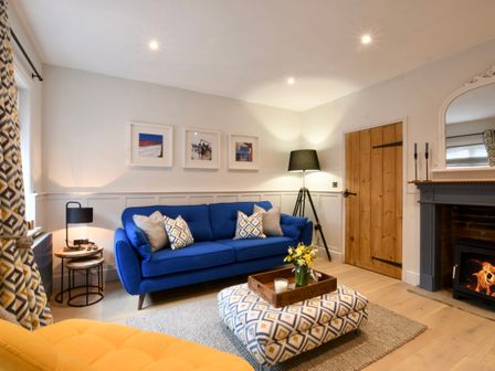 A living room with a blue sofa patterned ottoman wooden door and fireplace at Arlo Cottage Orford