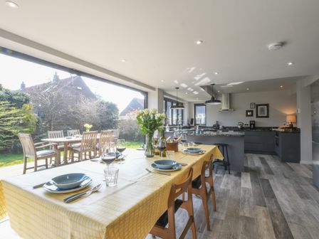 A kitchen and dining area with a yellow tablecloth on the dining table and outdoor seating visible through large open windows at Lavvande Walberswick