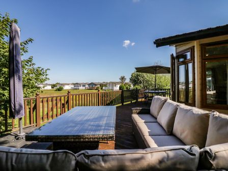An outdoor wooden deck with cushioned seating, a glass table, and an umbrella at The Hide Out in Aldeburgh