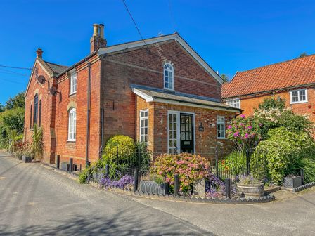 A brick house with a garden and flowers by the road at Chapel Cottage Newbourne Near Woodbridge