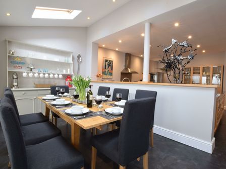 A dining area with a wooden table set with dishes and wine glasses surrounded by dark chairs at Regatta Lookout in Aldeburgh