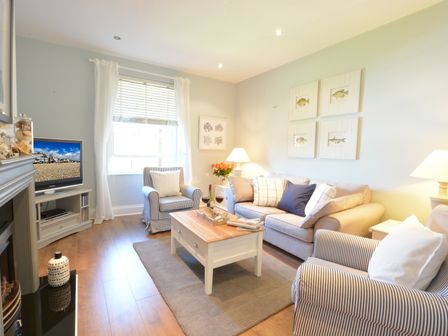 A living room with a sofa two armchairs a coffee table a television and framed fish pictures on the wall at High Tide Crabbe Street Aldeburgh in Aldeburgh