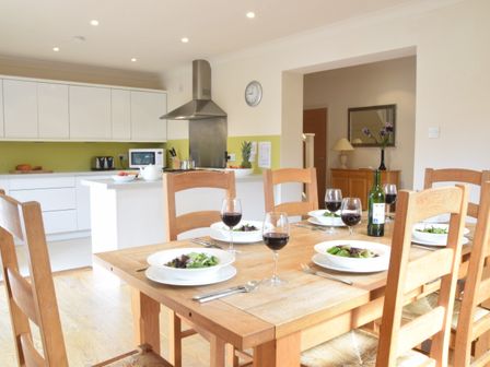 A dining table set with plates of salad and glasses of red wine in a kitchen with white cabinets and green backsplash at Peach House Aldeburgh