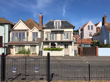 A row of houses with balconies and chimneys along a street behind a black metal fence at Tamarisk Aldeburgh in Aldeburgh
