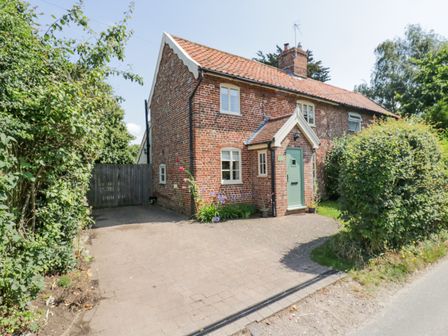 A brick cottage with a tiled roof and green door next to a driveway and garden at Shoemakers Cottage Friston