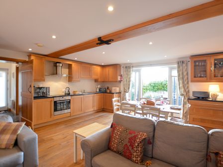 An open plan kitchen and dining area with wooden cabinets, dining table with chairs, and sofas at Three Chantry Barns, Orford