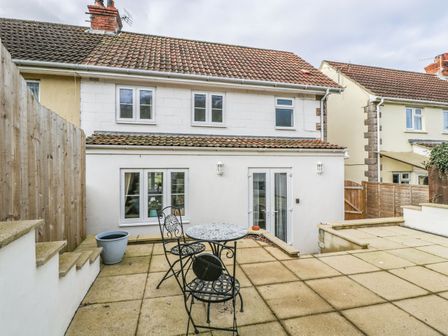 An outdoor patio area with a small round table and two chairs in front of a white two-story house at Celia's View Aller near Langport