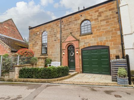 Stone building with green garage door and entrance door with steps and white bench in front at Riverside Chapel in Great Ayton