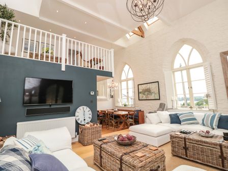A living room with sofas and a TV mounted on a dark wall under a loft area at The Old Chapel in Dittisham