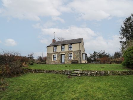 A two-story house with stone and plaster walls on a grassy hillside with trees nearby at Ceunant near Newport