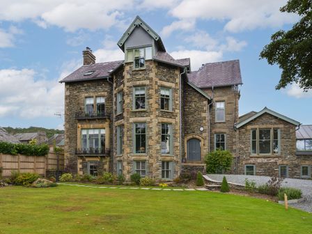A stone building with multiple windows and a gray door surrounded by a green lawn at Wansfell at Lipwood House in Windermere