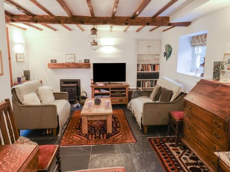 A living room with two armchairs a wooden coffee table a television and bookshelves at Naunton Cottage in Lyme Regis