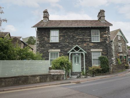 A stone cottage with two chimneys and a green door on a street at Rose Cottage in Ambleside