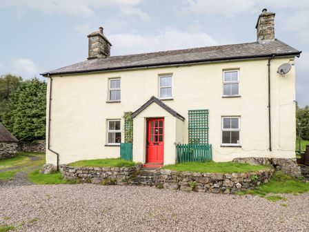 A two story house with a red front door gravel driveway and stone wall at Gwengraig in Brithdir near Dolgellau