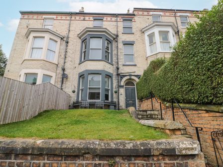 An exterior view of a brick townhouse with bay windows a green door stairs on the right and grass in front at Westbourne House in Scarborough