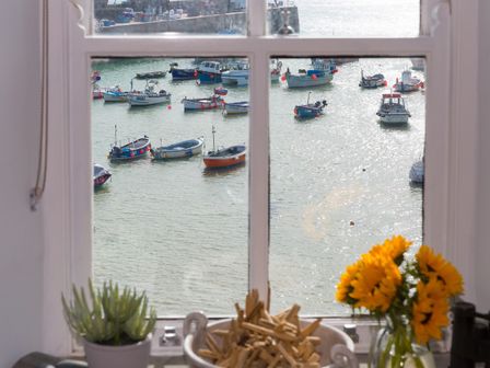 A window view of boats on water with plants and sunflowers on the windowsill at 5 St Brigids in St Ives