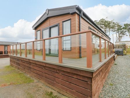 A wooden cabin with glass railing on a raised platform surrounded by gravel and grass at Starfish Retreat in Little Haven near Broad Haven