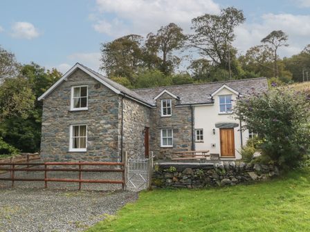 A stone and white two-story cottage with a wooden door and a small fenced yard at Tyn Llwyn in Eisingrug near Harlech