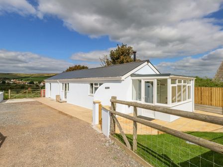 A single story white building with a grey roof and glass entrance surrounded by a wooden fence at Cliff Barn in Burton Bradstock